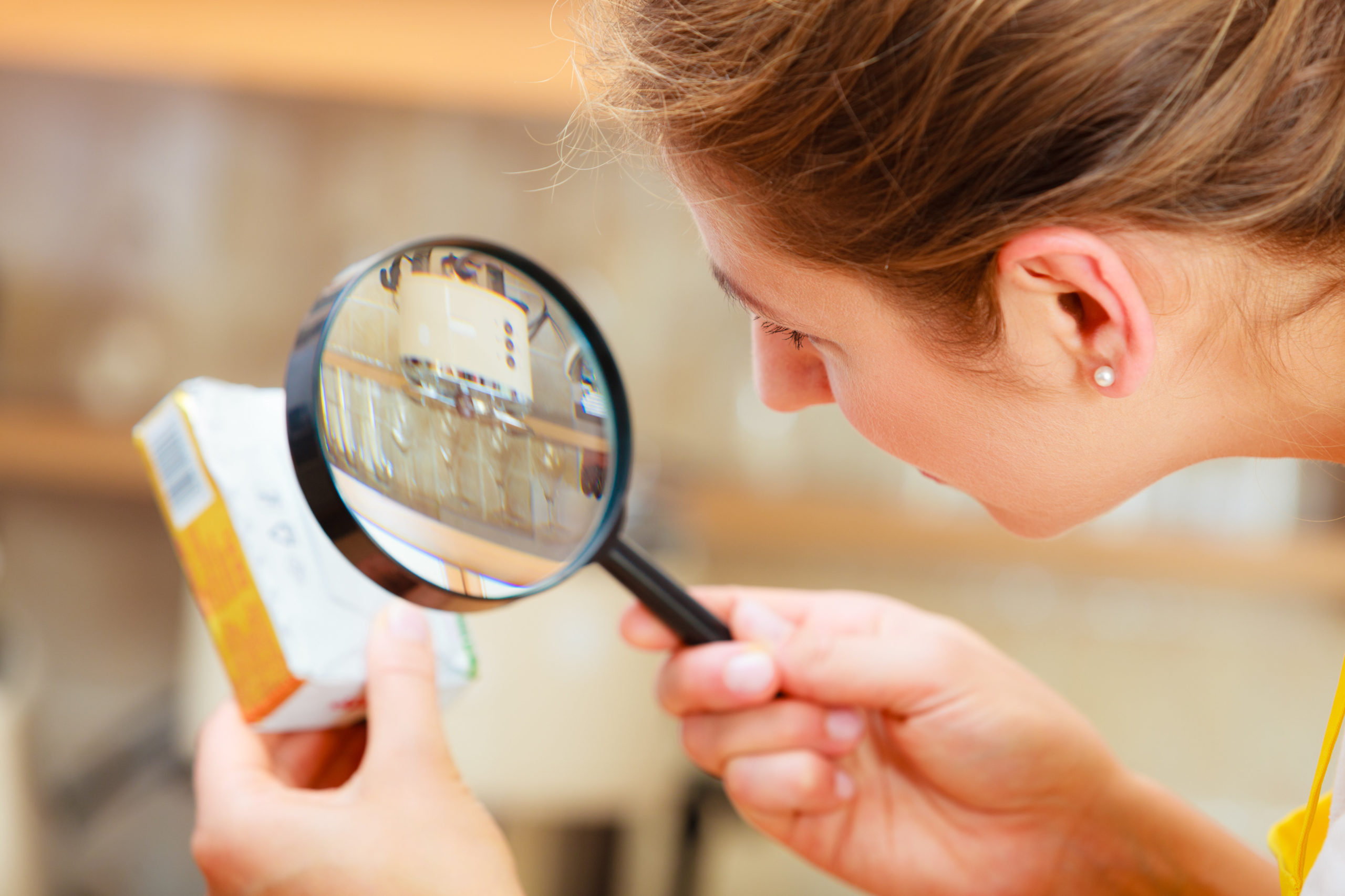 woman inspecting package ingredients with magnifying glass